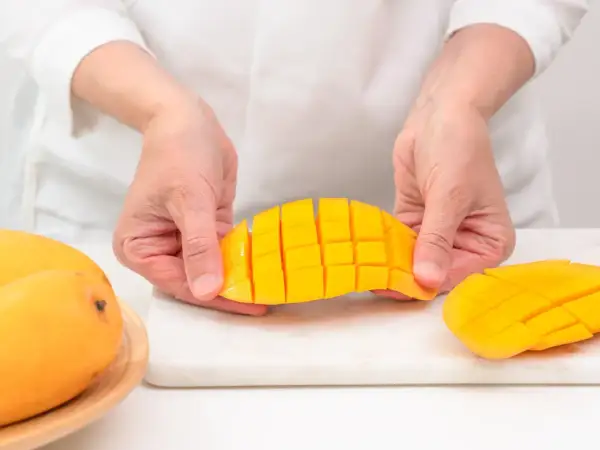 Ręce kroją mango na kostki. Czy koty mogą jeść mango? To pytanie nurtuje wielu właścicieli.